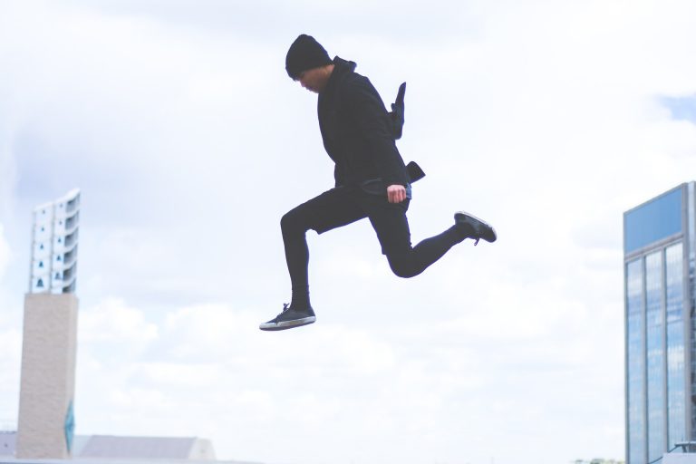 Man dressed in all black jumping through the air with buildings in the background