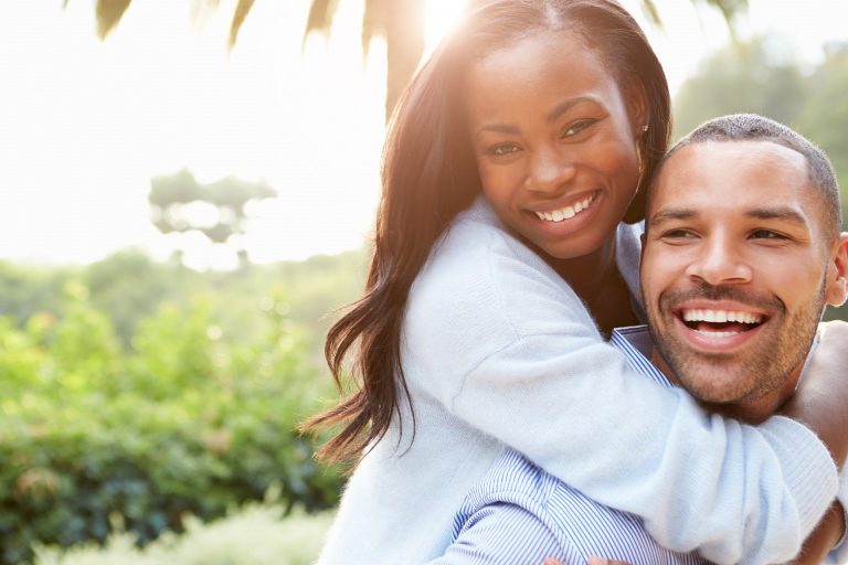 African American man and woman smiling with beautiful tropical scenery behind them