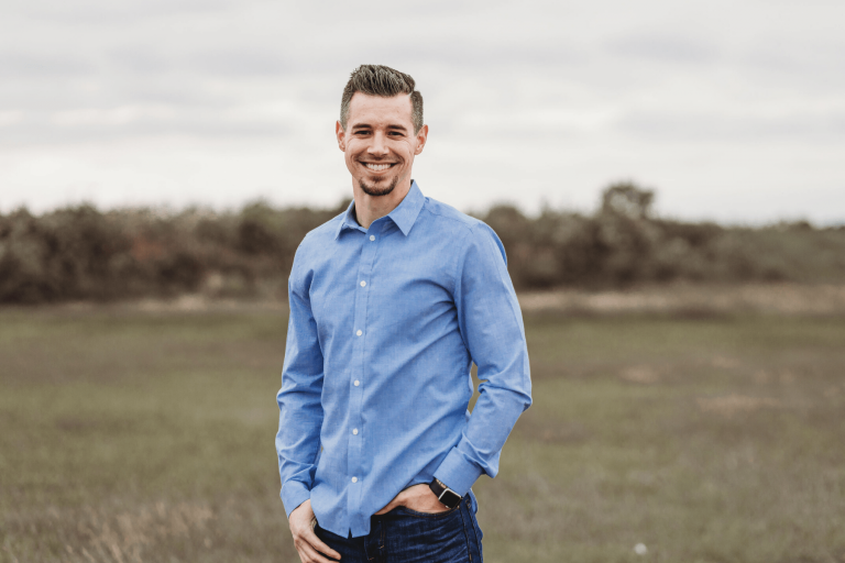 Man in blue button down short and blue jeans standing in a field.