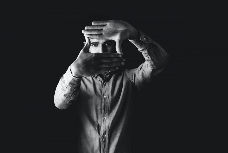 Black and white photo of a man in a button down shirt looking through a square he made with his hands