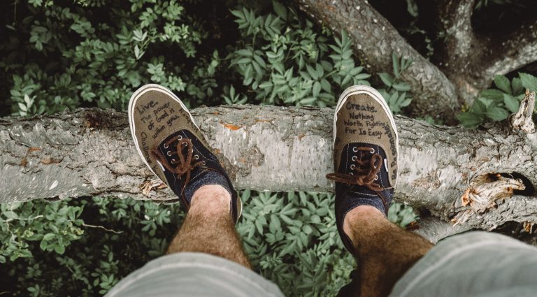 The legs of a man standing on the edge of a cliff with motivational quotes written on his shoes
