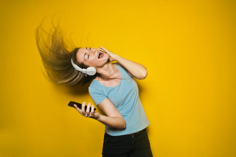 Women in front of a yellow background whipping her hair while listening to music